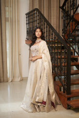 A woman wearing a traditional Indian outfit with a cream-colored embroidered kurta and a matching dupatta, standing in front of an indoor staircase Pista Floral Jaal Stone & Pearl Lehenga Set by MeenaGurnam